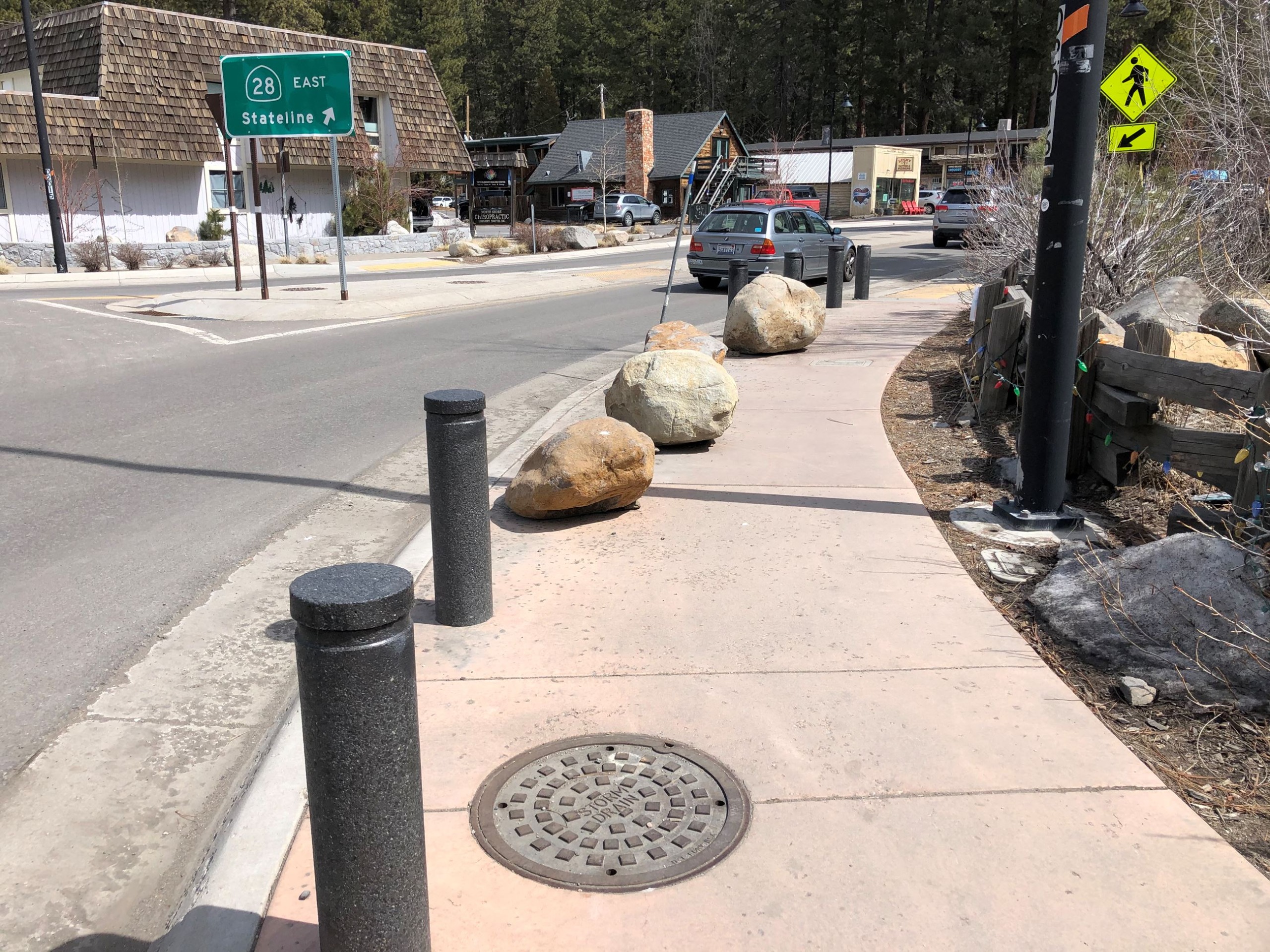 An image of bollards and boulders on a sidewalk near a roundabout.