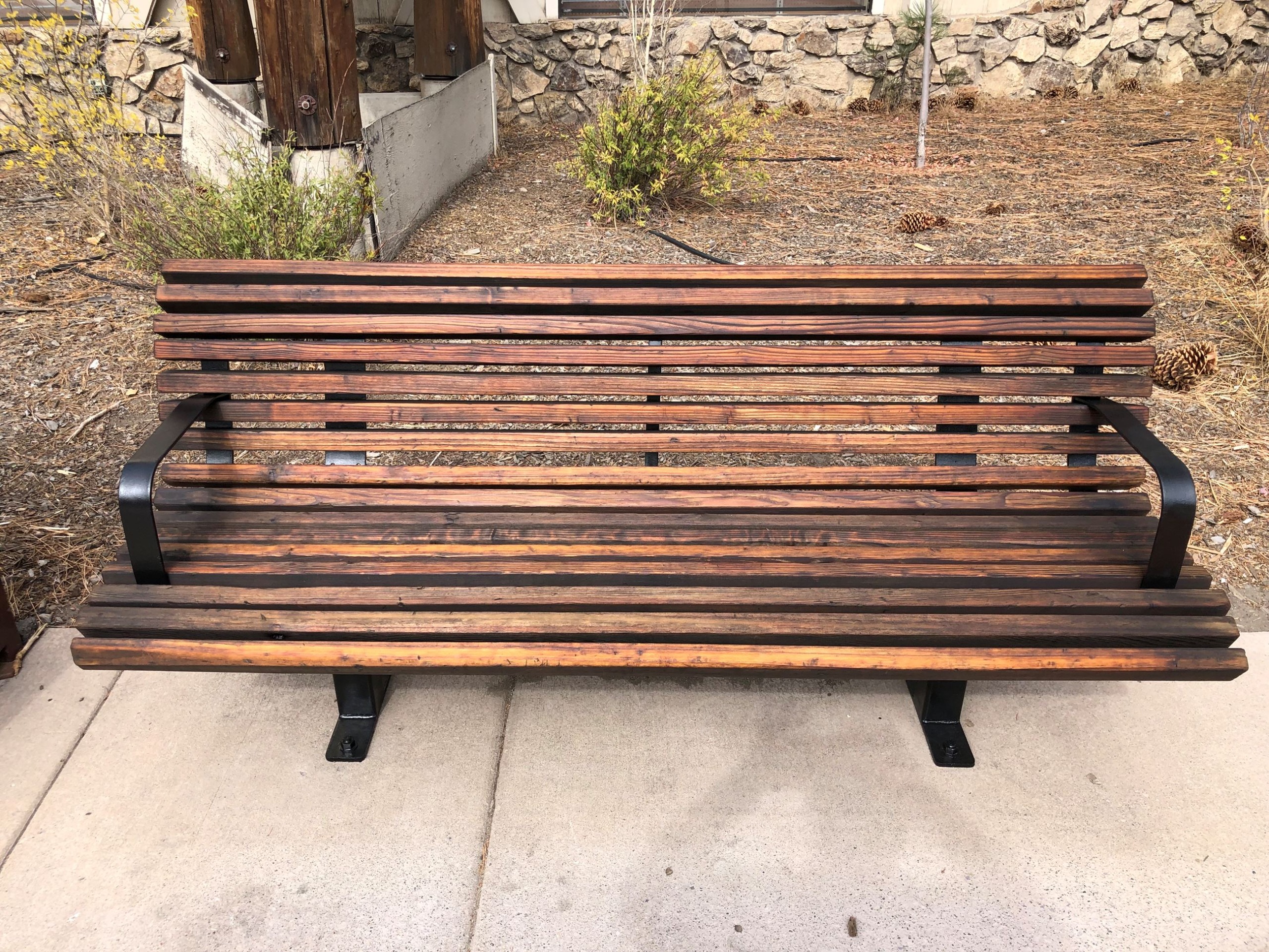 A dark wooden bench with black metal legs on concrete in Kings Beach. 
