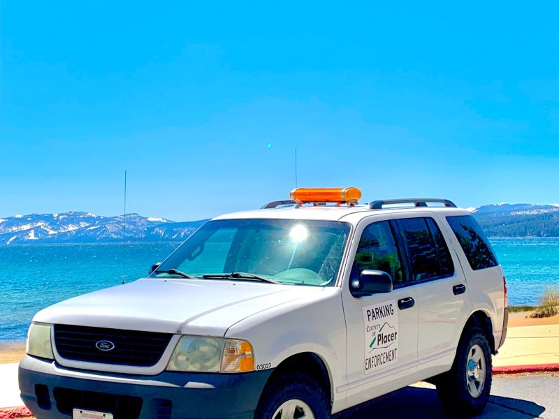 A white SUV with parking enforcement decals in front of Lake Tahoe. 